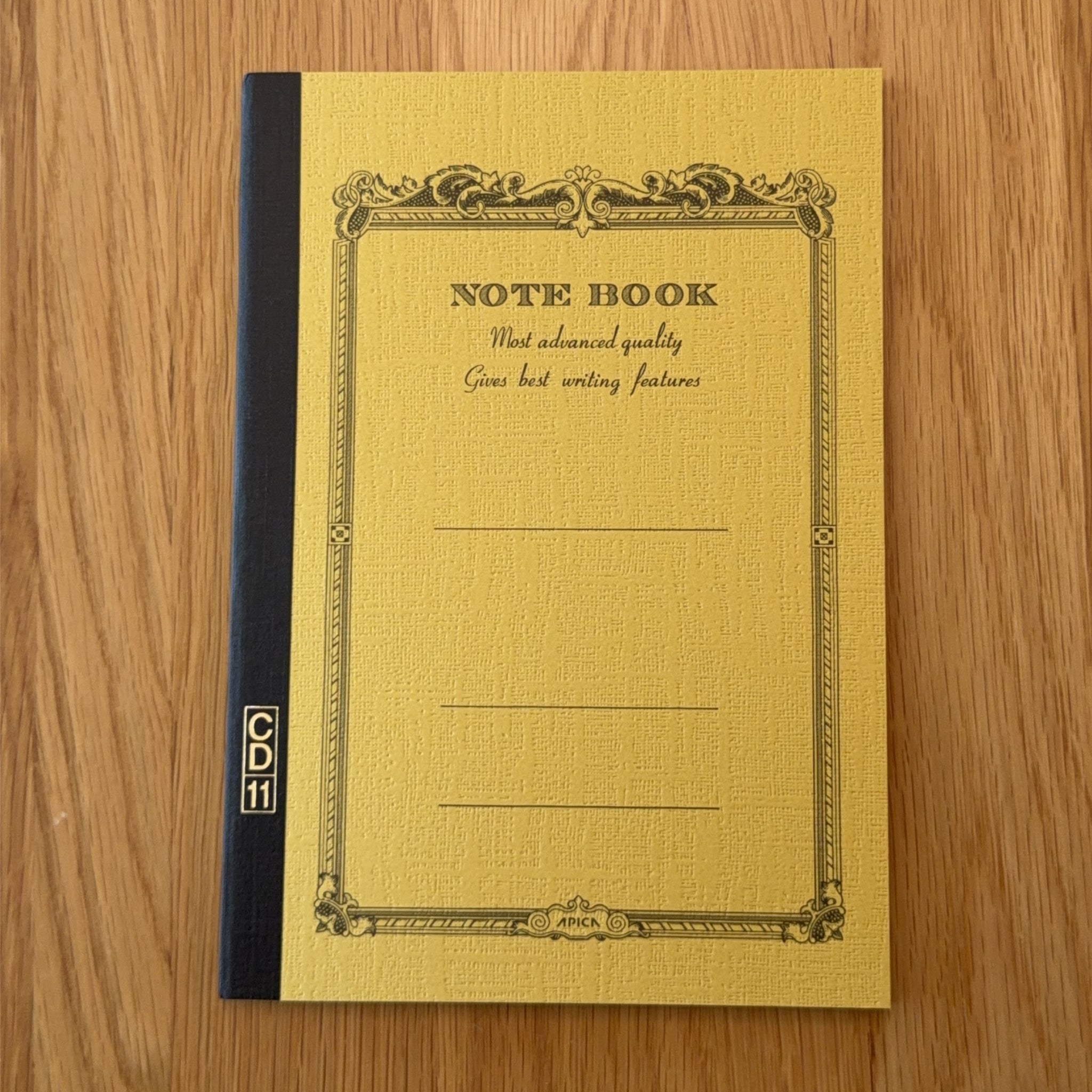 Apica CD Notebook A5 in Mustard, shown flat on a wooden surface