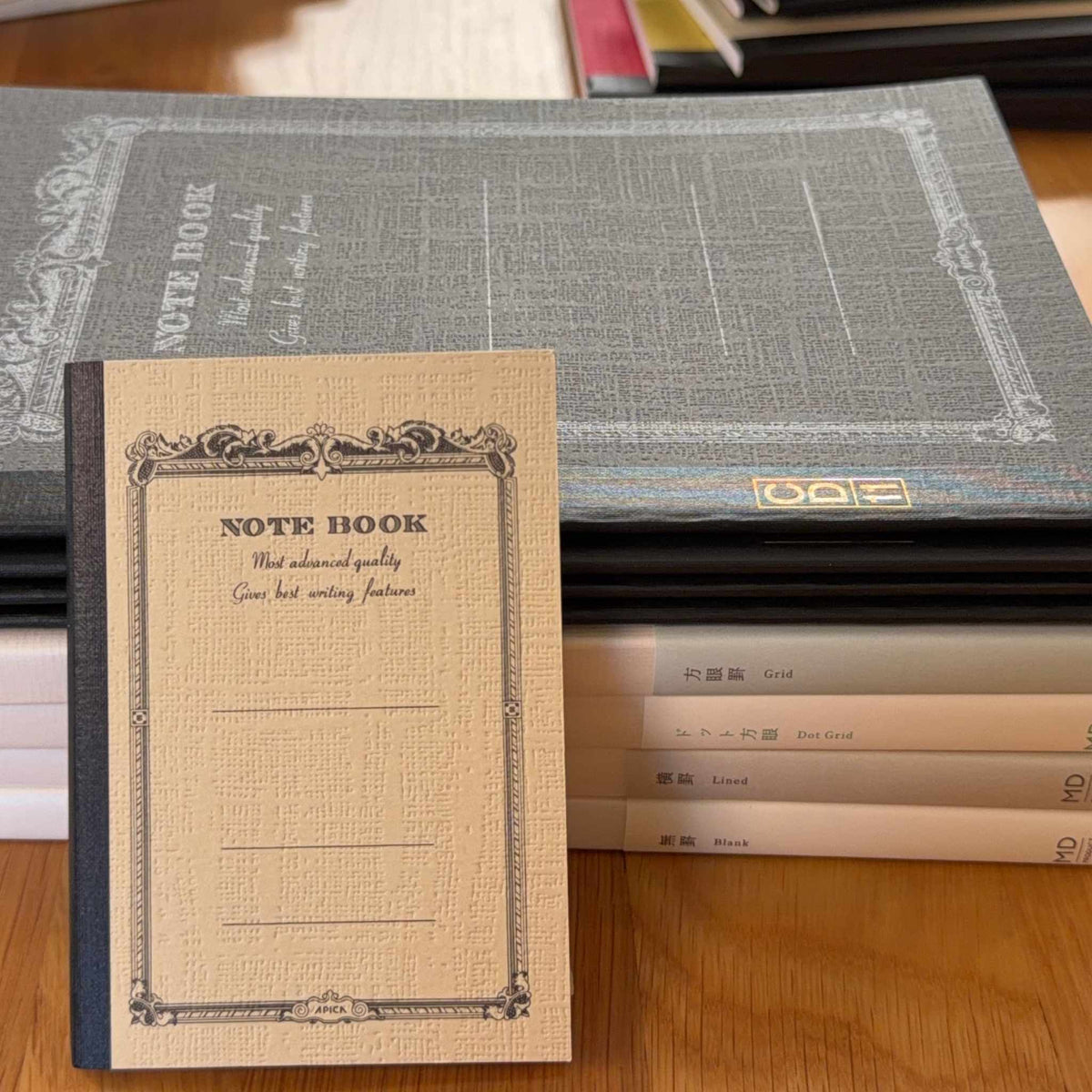 Apica CD and Midori MD notebooks arranged together, showing the Apica notebook cover design and MD notebook spine labels for Grid, Dot Grid, Lined, and Blank ruling