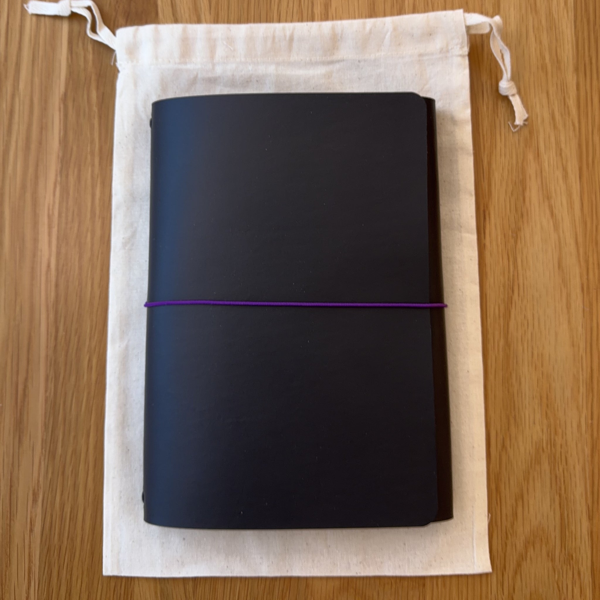 Journey A5 leather notebook cover in Black, closed, resting on its Floramoon cotton dust bag