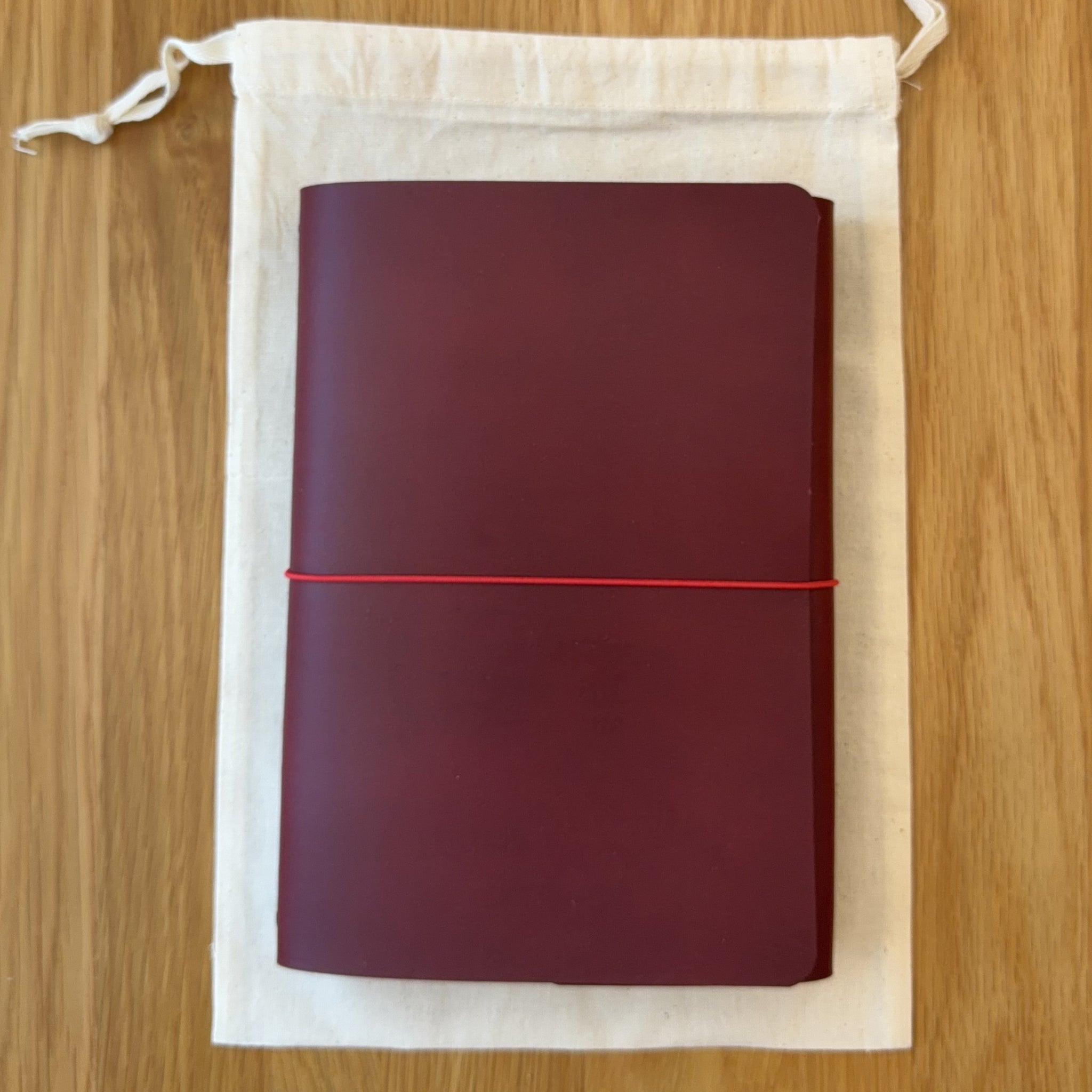 Journey A5 leather notebook cover in Bordeaux, closed, resting on its Floramoon cotton dust bag