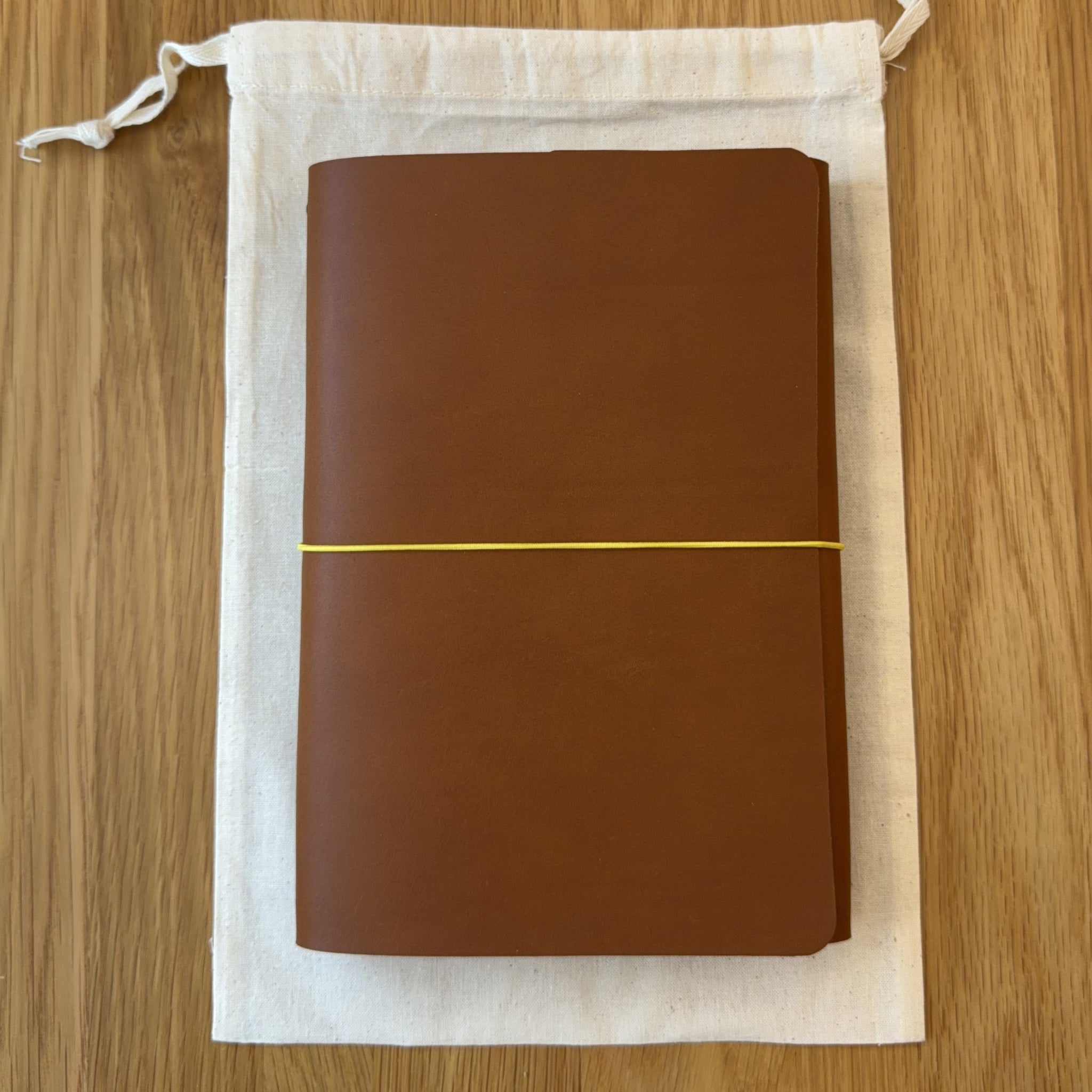 Journey A5 leather notebook cover in Cognac, closed, resting on its Floramoon cotton dust bag