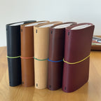 Five Journey A6 leather notebook covers in Black, Cognac, Natural, Tobacco, and Bordeaux, standing side by side