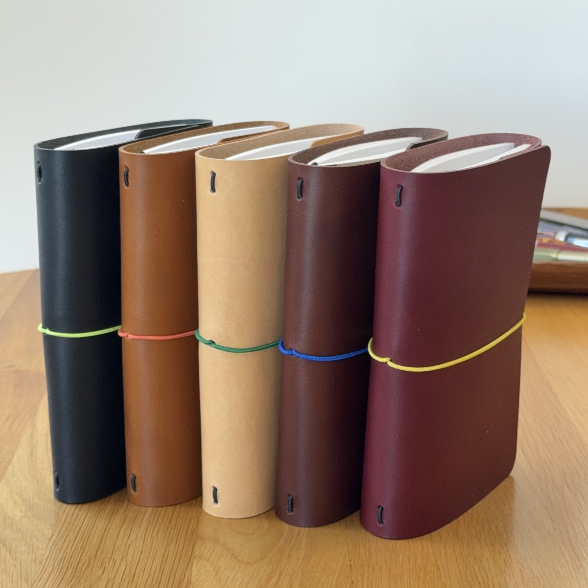 Five Journey A6 leather notebook covers in Black, Cognac, Natural, Tobacco, and Bordeaux, standing side by side