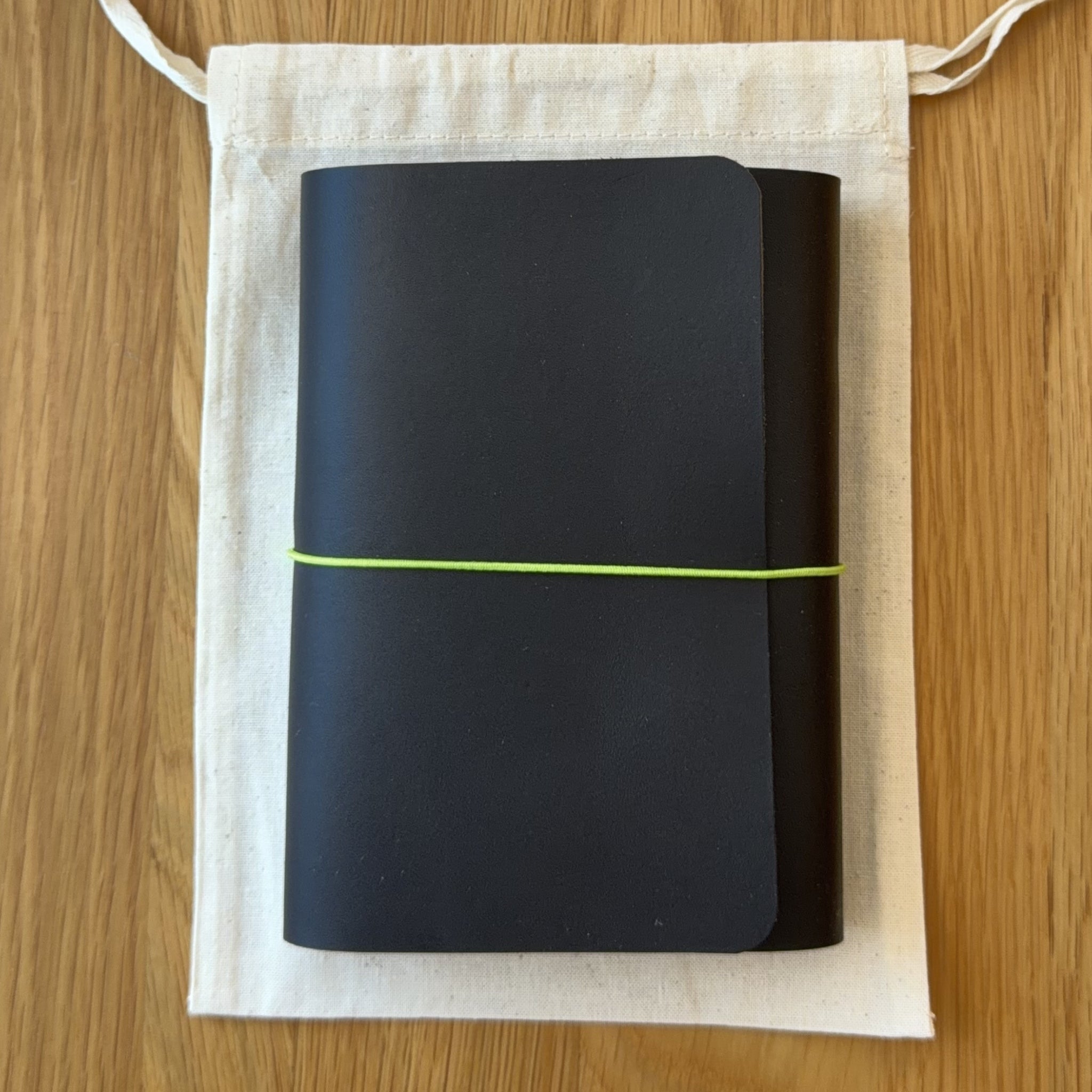 Journey A6 leather notebook cover in Black, closed, resting on its Floramoon cotton dust bag