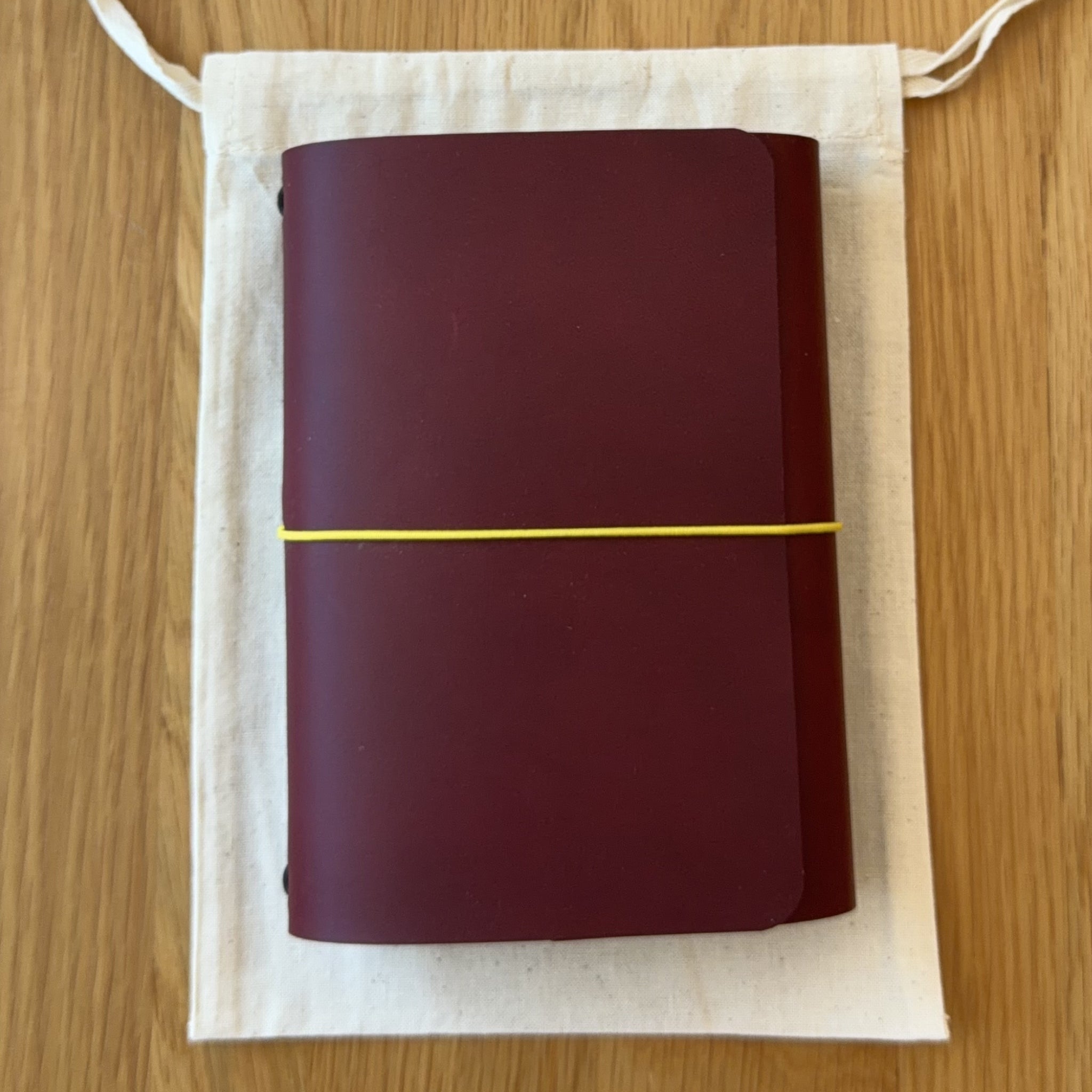 Journey A6 leather notebook cover in Bordeaux, closed, resting on its Floramoon cotton dust bag