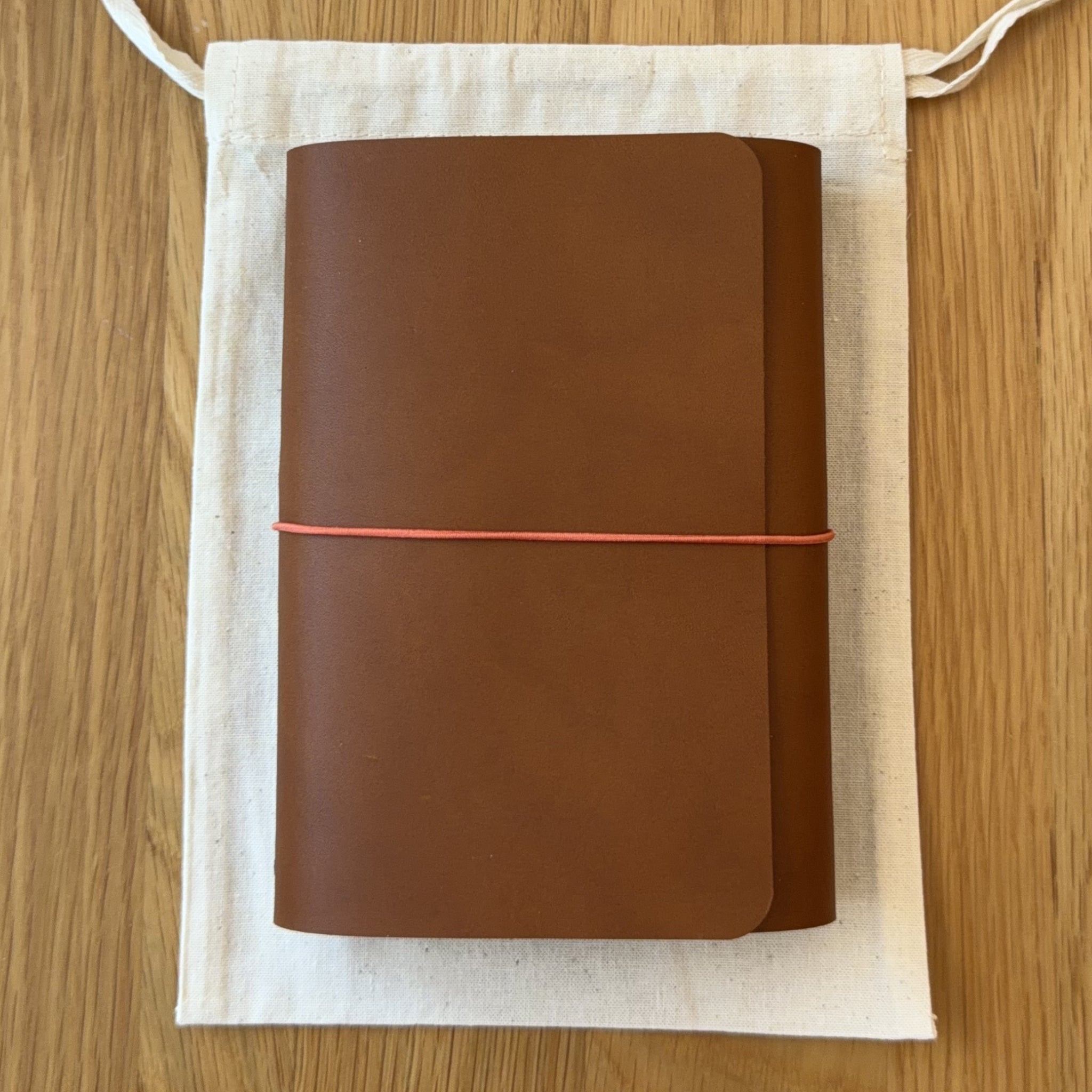 Journey A6 leather notebook cover in Cognac, closed, resting on its Floramoon cotton dust bag
