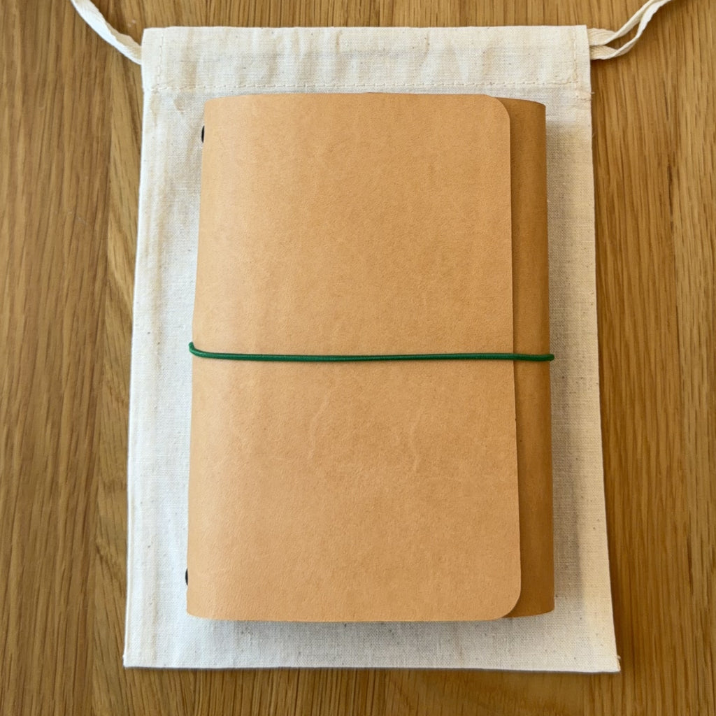 Journey A6 leather notebook cover in Natural, closed, resting on its Floramoon cotton dust bag