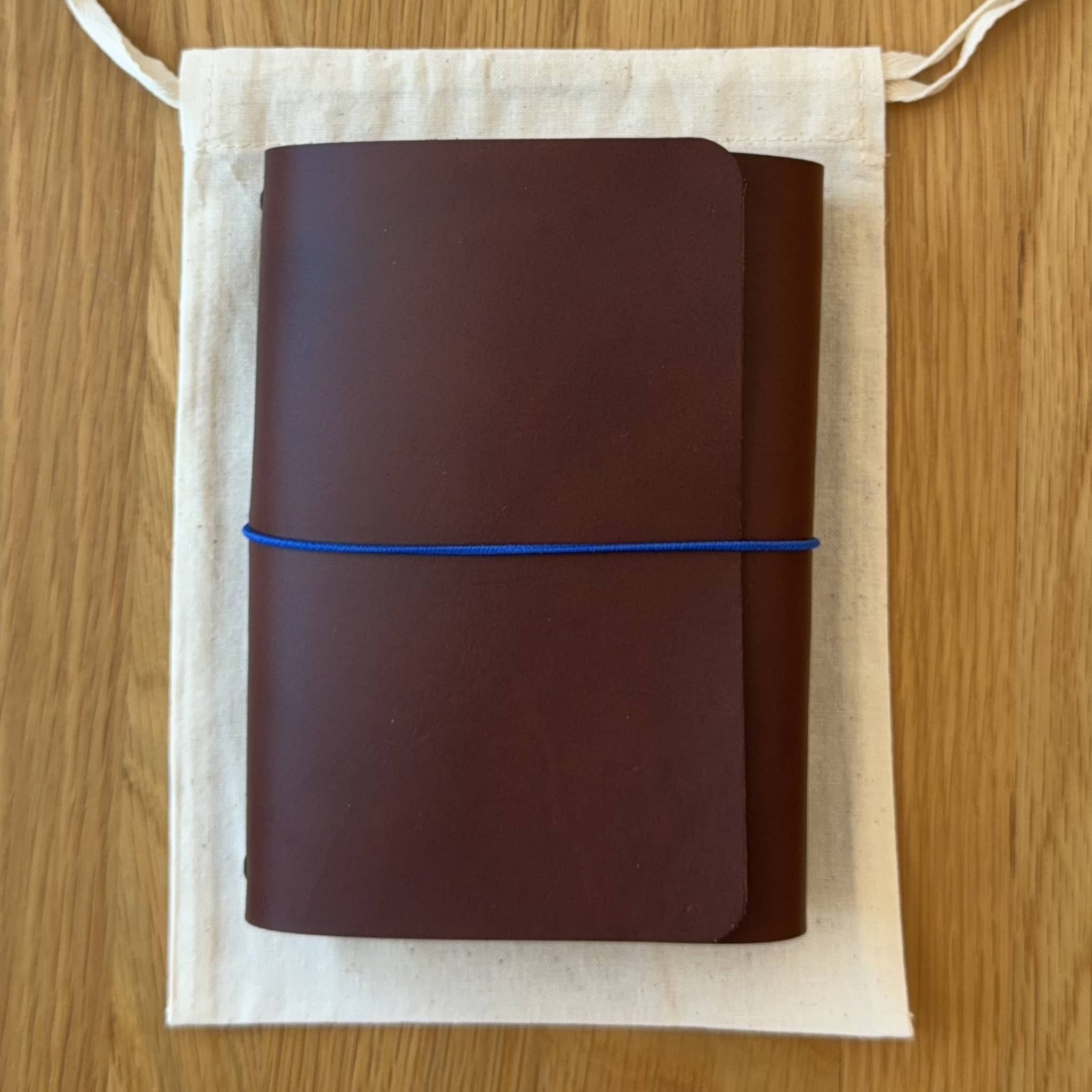 Journey A6 leather notebook cover in Tobacco, closed, resting on its Floramoon cotton dust bag