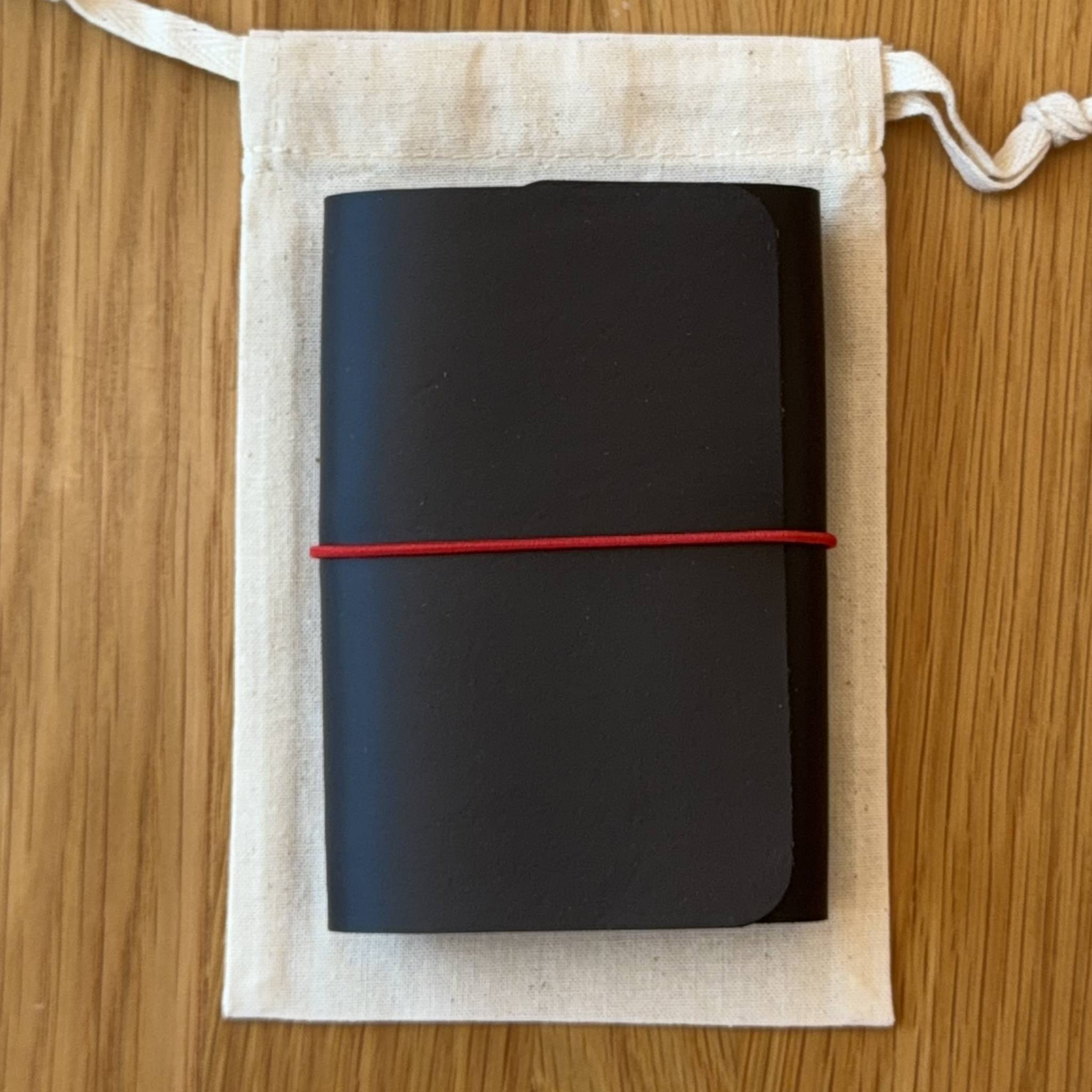 Journey A7 leather notebook cover in Black, closed, resting on its Floramoon cotton dustbag