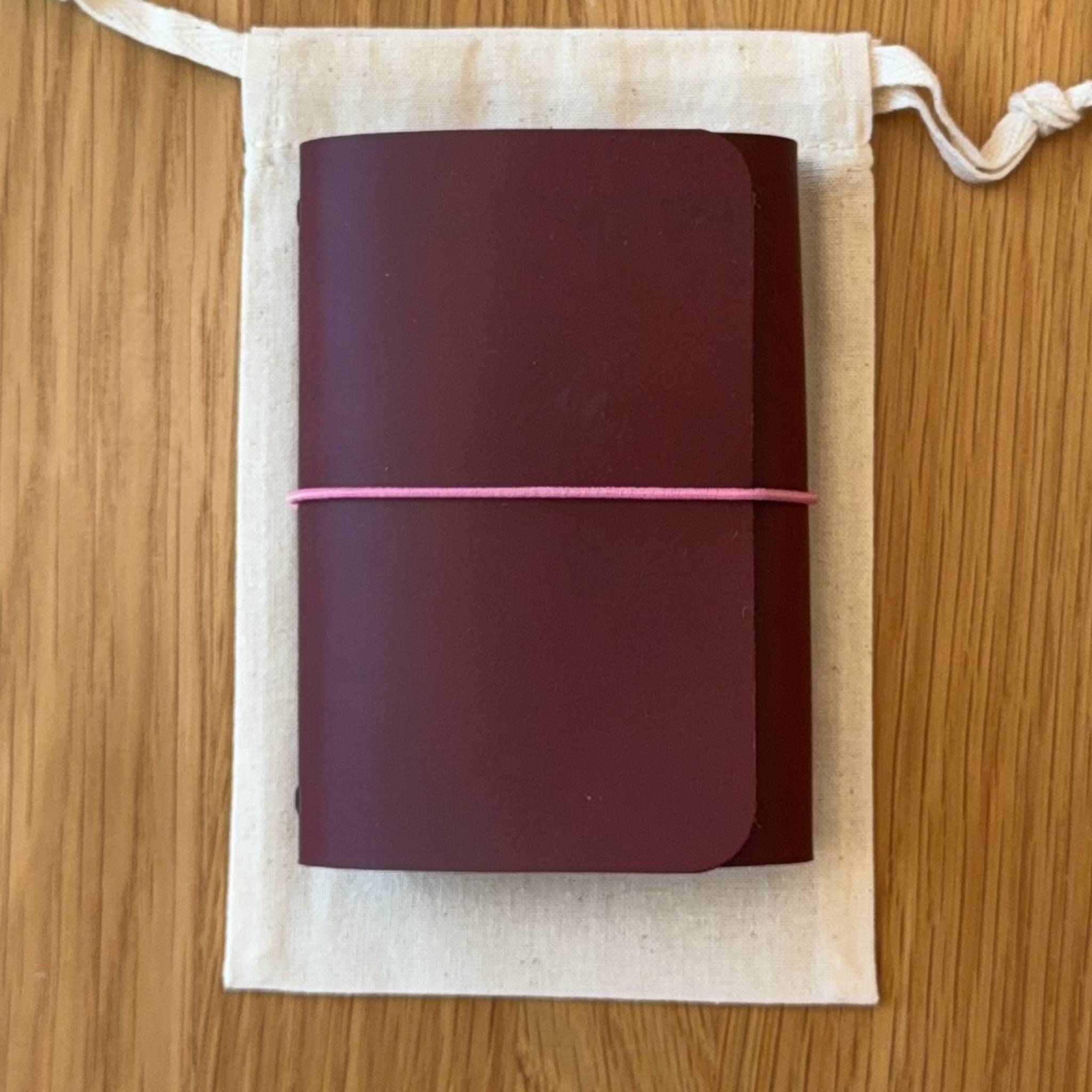 Journey A7 leather notebook cover in Bordeaux, closed, resting on its Floramoon cotton dustbag