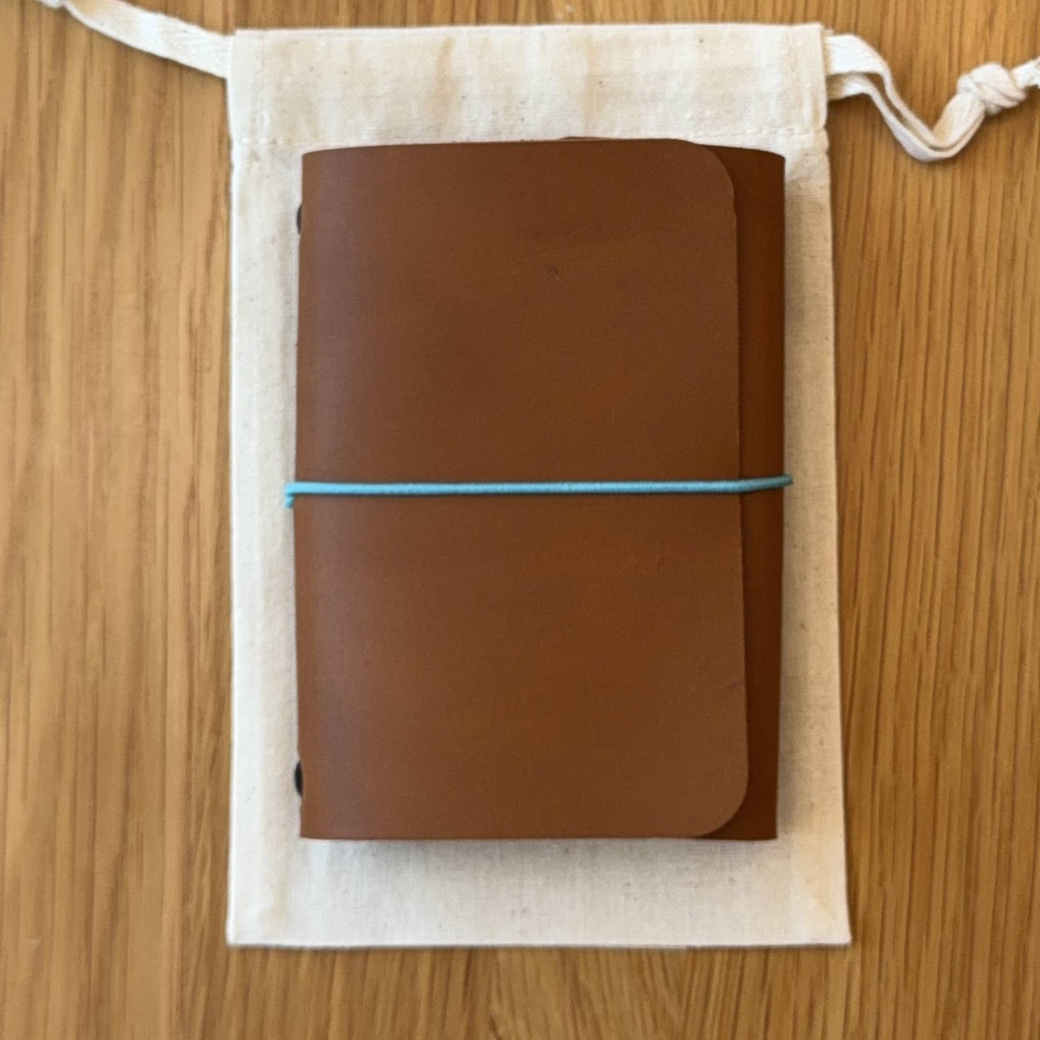 Journey A7 leather notebook cover in Cognac, closed, resting on its Floramoon cotton dust bag