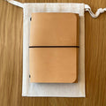 Journey A7 leather notebook cover in Natural, closed, resting on its Floramoon cotton dust bag