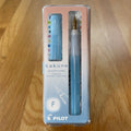 Pilot Kakuno Madoromi Fountain Pen in Light Blue, shown in its original packaging on a wooden surface, with the translucent barrel and gold nib visible through the case