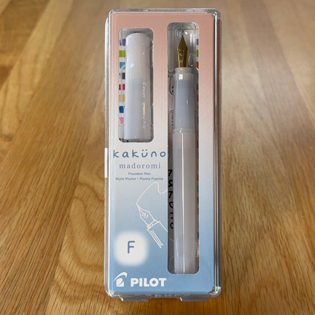 Pilot Kakuno Madoromi Fountain Pen in White, shown in its original packaging on a wooden surface, with the translucent barrel and gold nib visible through the case.