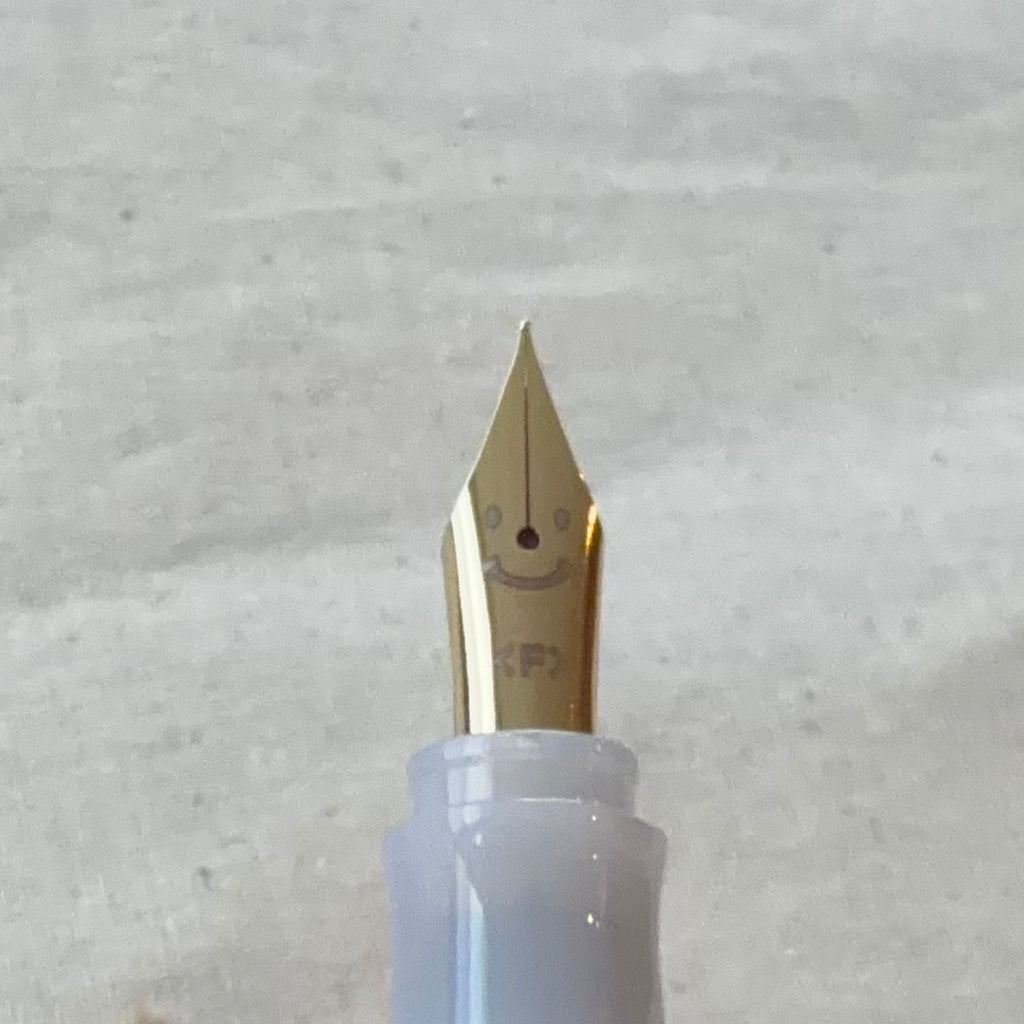 Close-up of a Pilot Kakuno Madoromi fountain pen nib in Fine point, gold-colored, with the translucent barrel visible behind it.