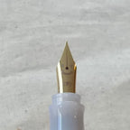 Close-up of a Pilot Kakuno Madoromi fountain pen nib in Fine point, gold-colored, with the translucent barrel visible behind it.