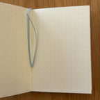 Midori MD Notebook A7 open to show the dot grid MD Paper and its bookmark string