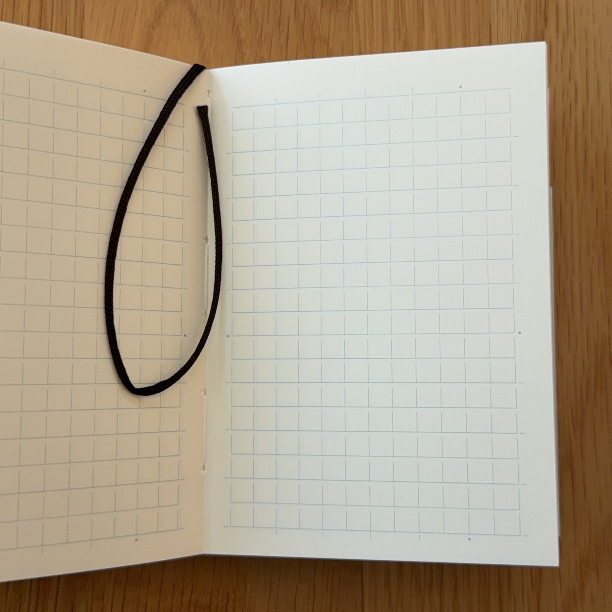 Midori MD Notebook A7 open to show the grid MD Paper and its bookmark string